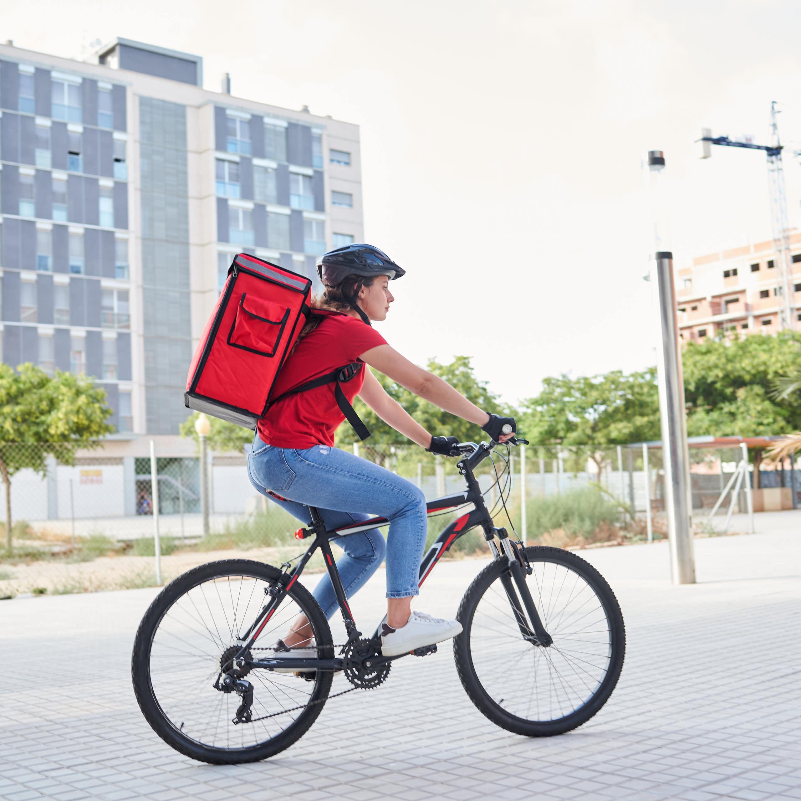 Una repartidora en bici amb la motxilla del repart a l'esquena.
