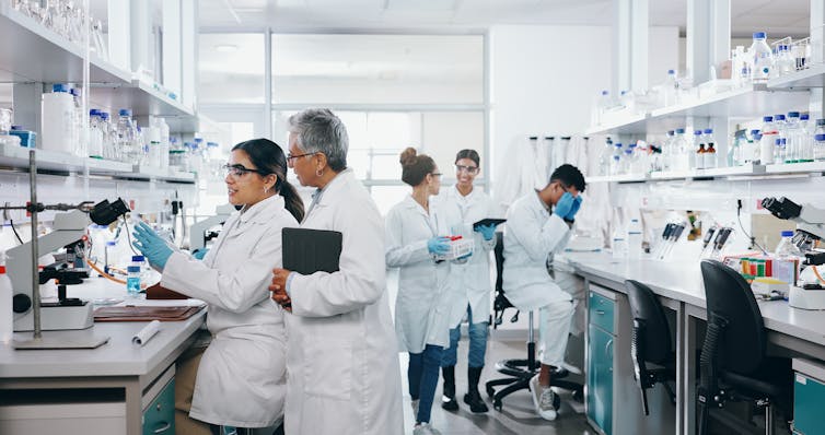 Group of people wearing white lab coats and protective eye equipment working in a lab