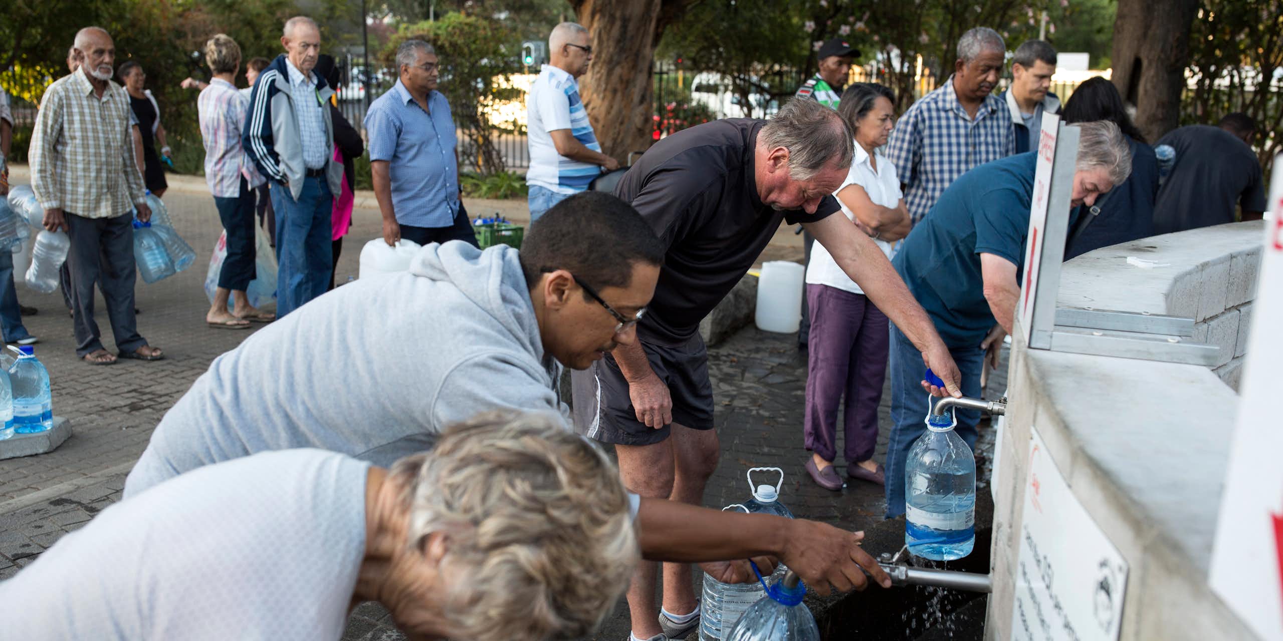 People of all backgrounds stand in line with jugs to fill with water.