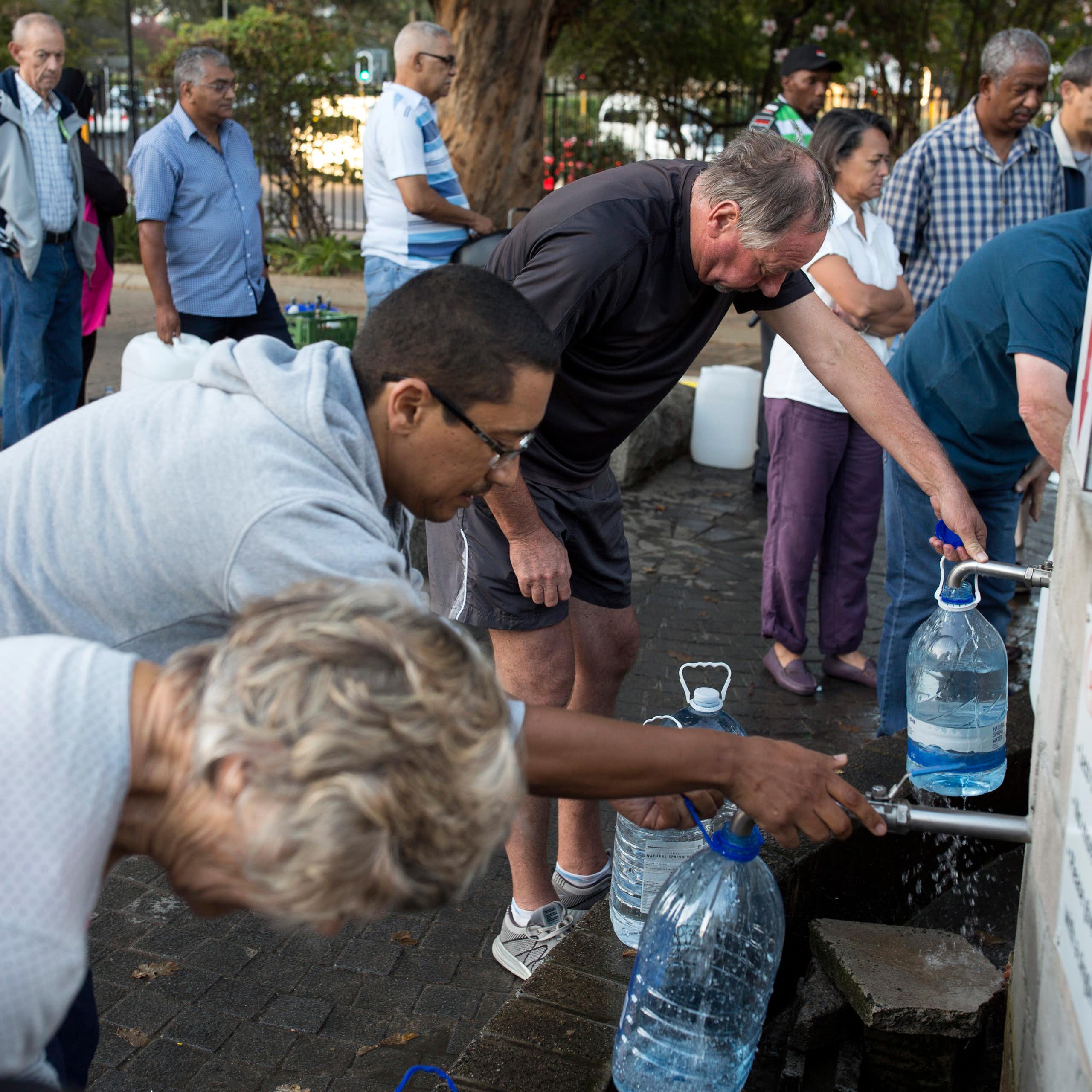 People of all backgrounds stand in line with jugs to fill with water.
