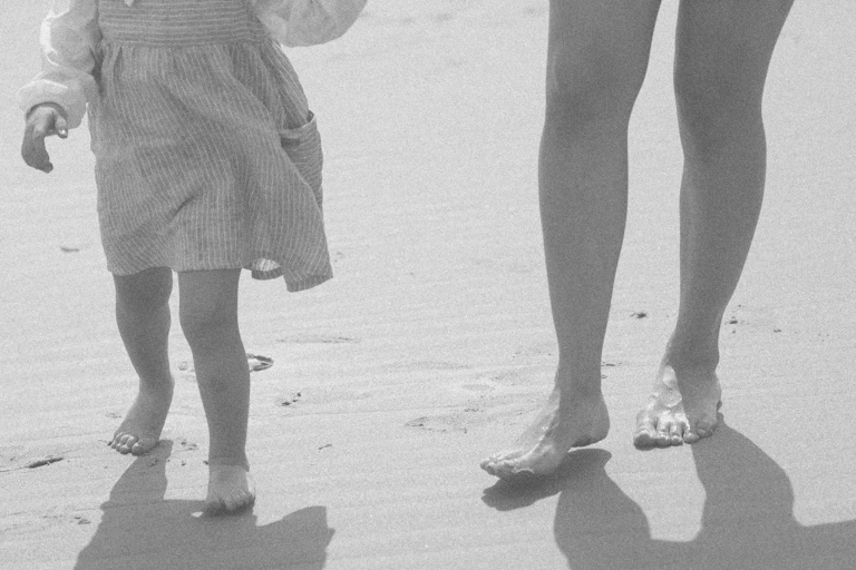 A view of a young girl and woman are seen from the waist down on a beach.