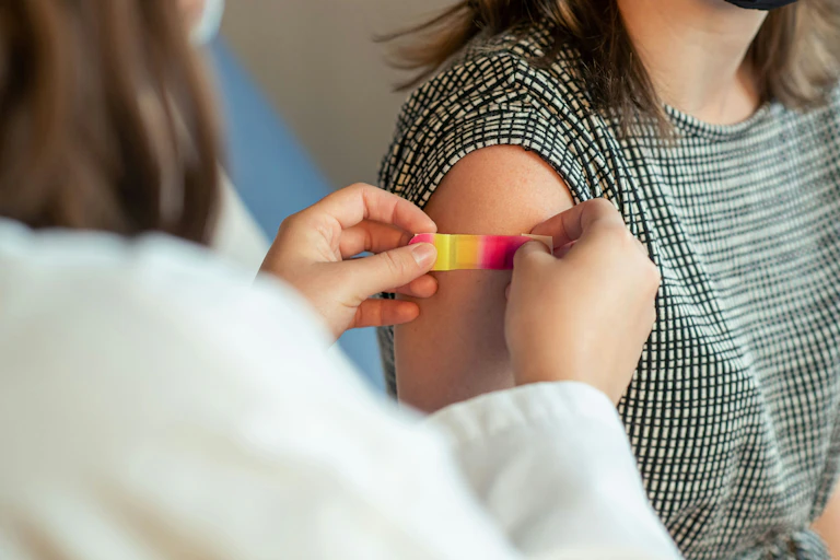 Cropped image of a health-care provider putting a bandage on a woman's upper arm after a shot