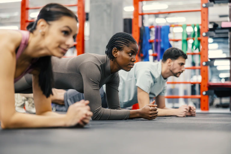 Three people holding plank position in a gym.
