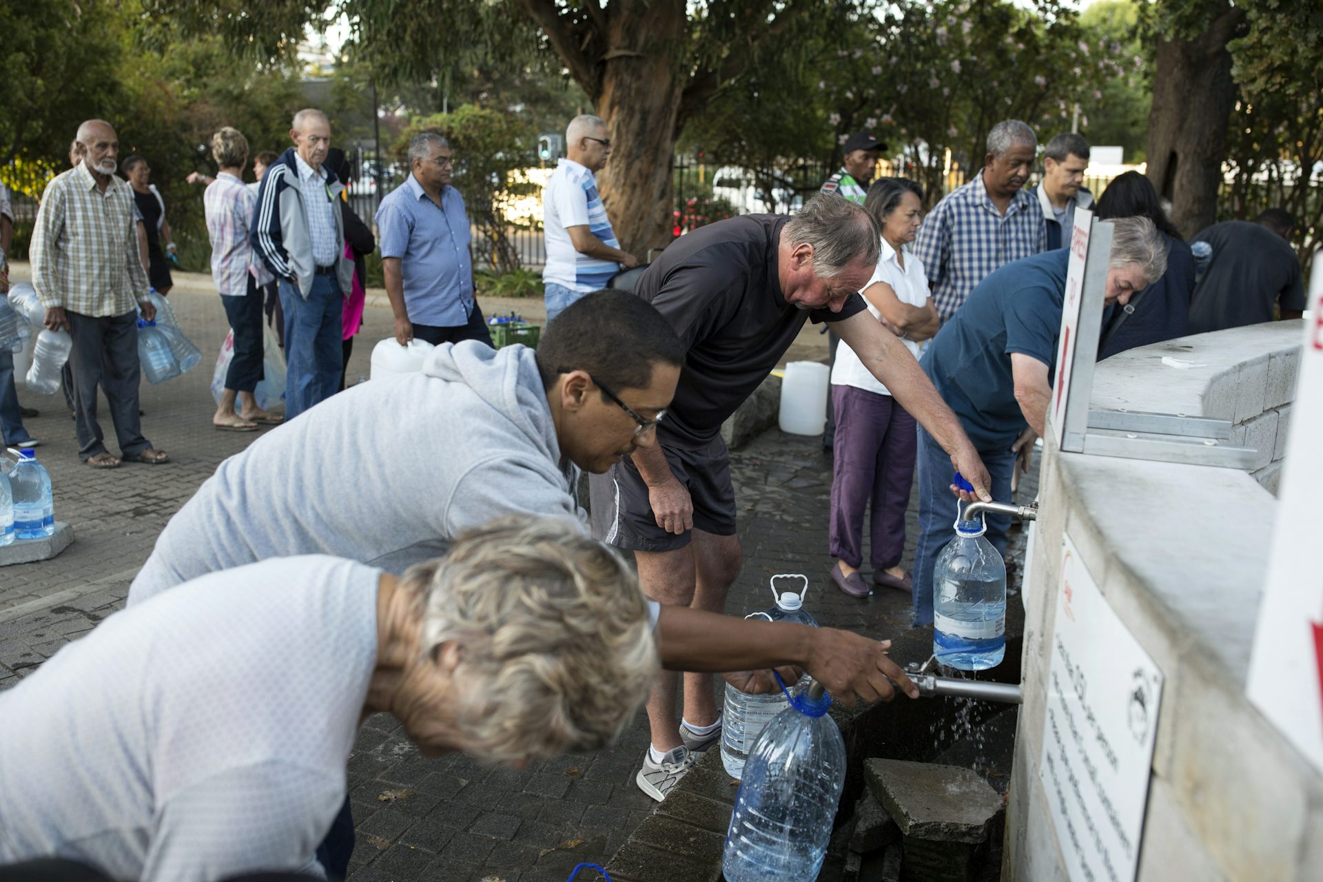 Personas hacen fila con jarras para llenarlas de agua.