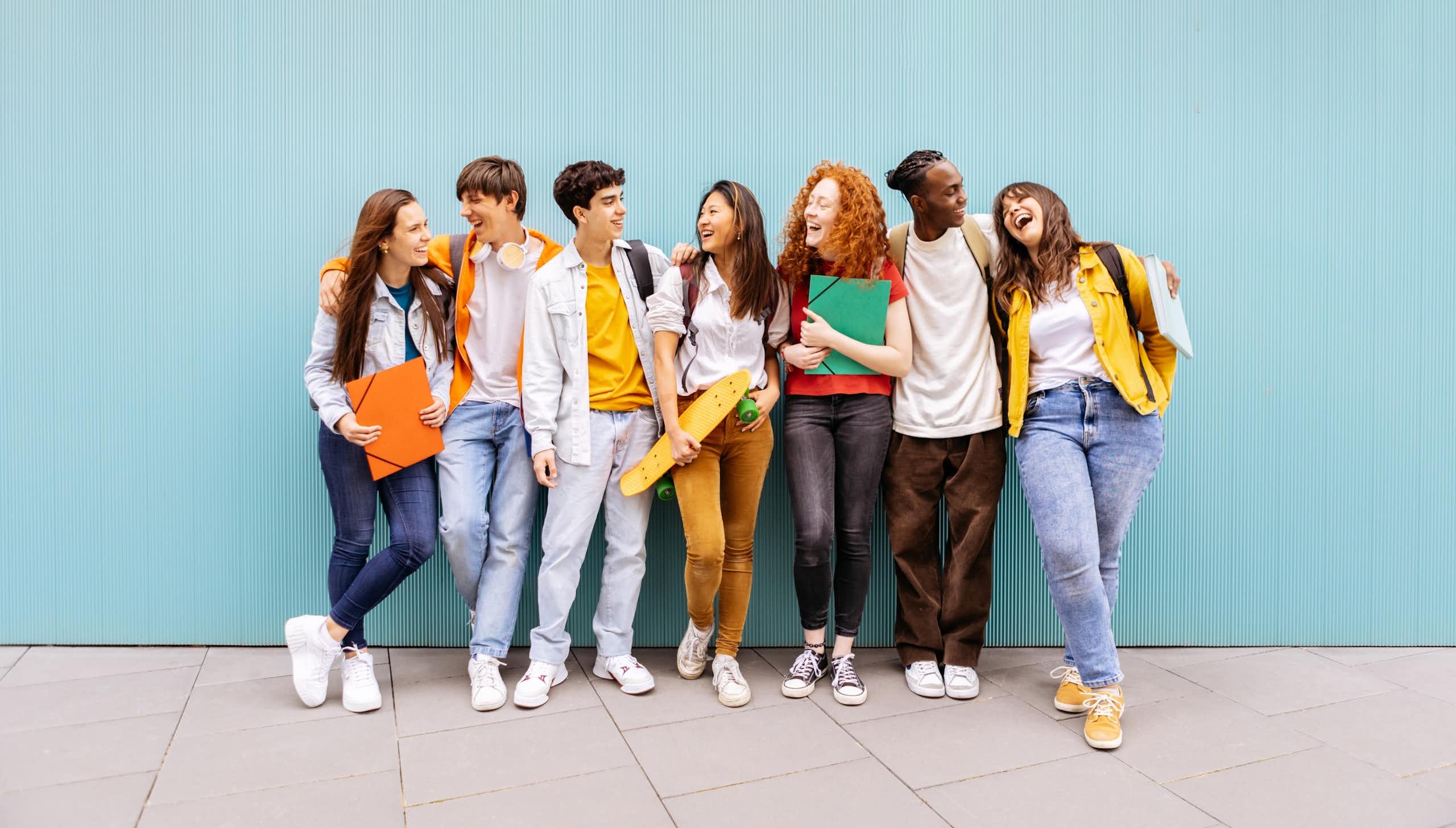 Un grup de joves s'abracen i riuen recolzats en una paret blava.