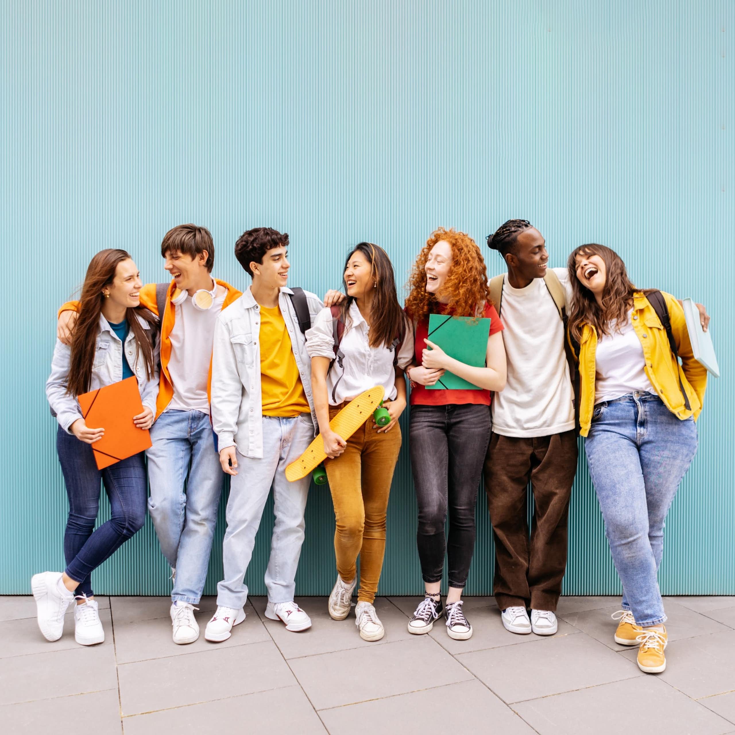 Un grup de joves s'abracen i riuen recolzats en una paret blava.