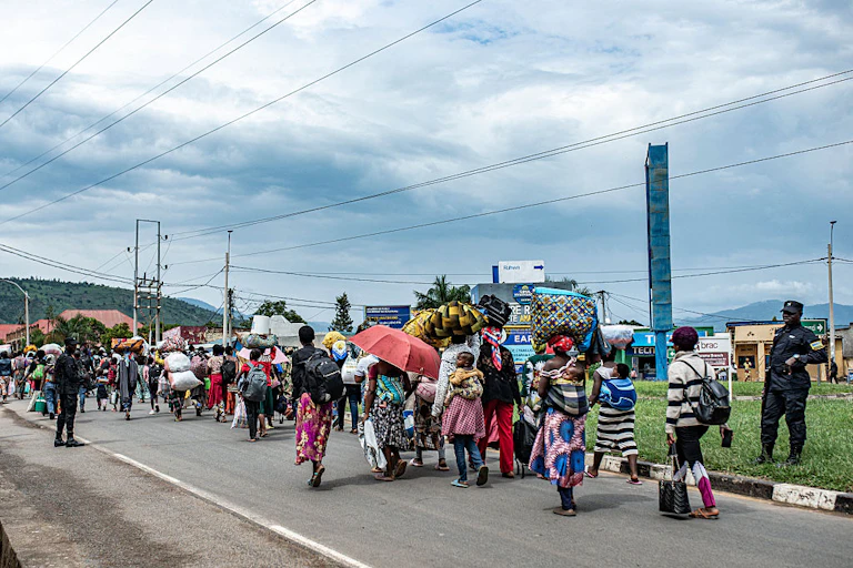 A group of people walking on a paved road carrying bags on their backs and heads.
