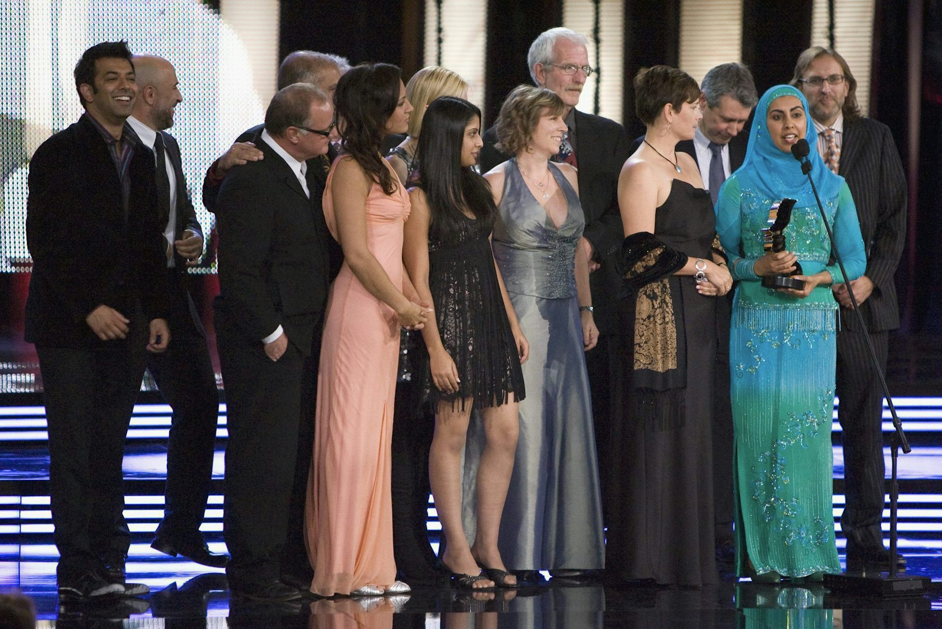 Las personas que se encuentran en el podio, incluidas mujeres con vestidos formales y una con hiyab, además de hombres con traje, reciben el premio.