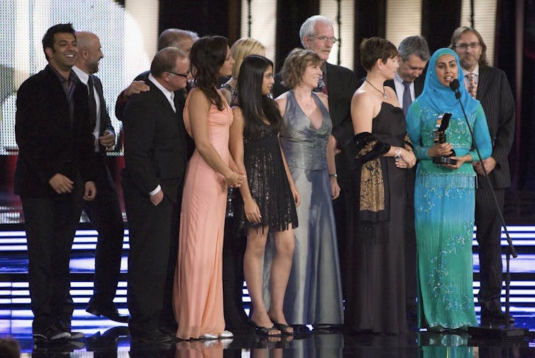 Rivalidad abrasadora: cómo las inversiones en contenido canadiense pueden dar sus frutos en el país y en el extranjero 3 Las personas que se encuentran en el podio, incluidas mujeres con vestidos formales y una con hiyab, además de hombres con traje, reciben el premio.