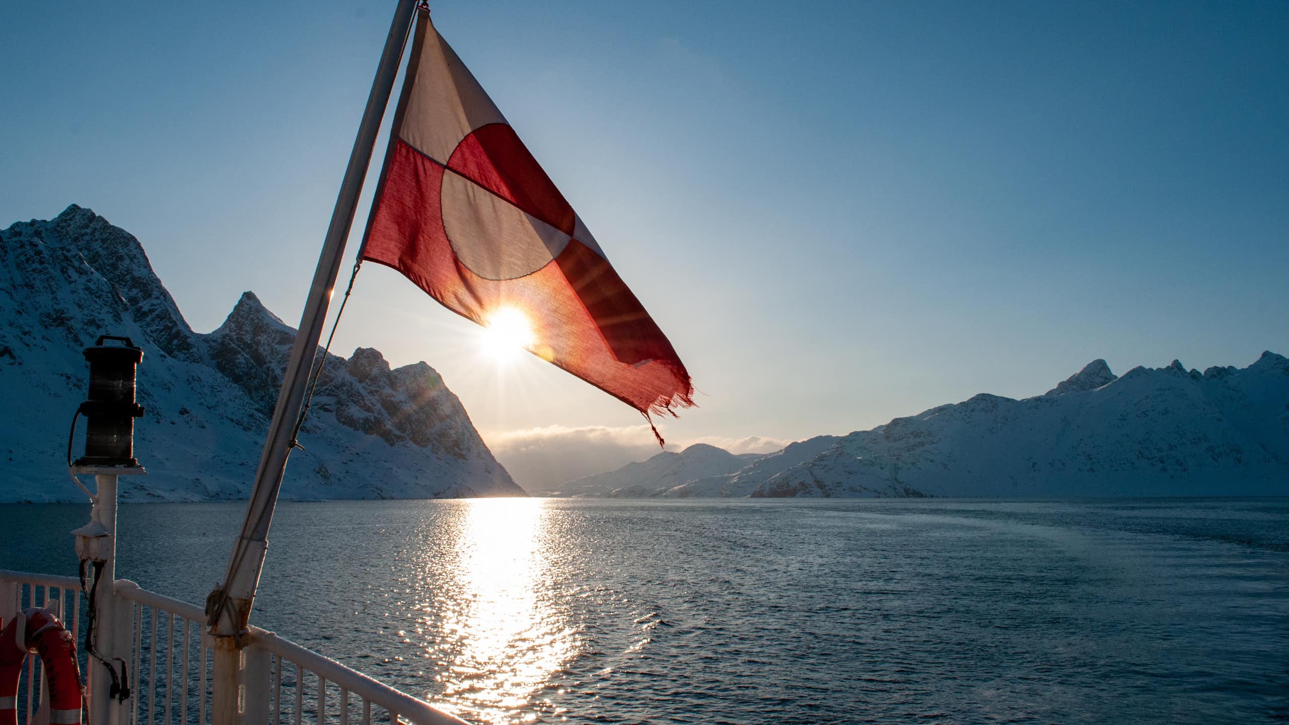 Flag of Greenland onboard a boat sailing among snow covered mountains