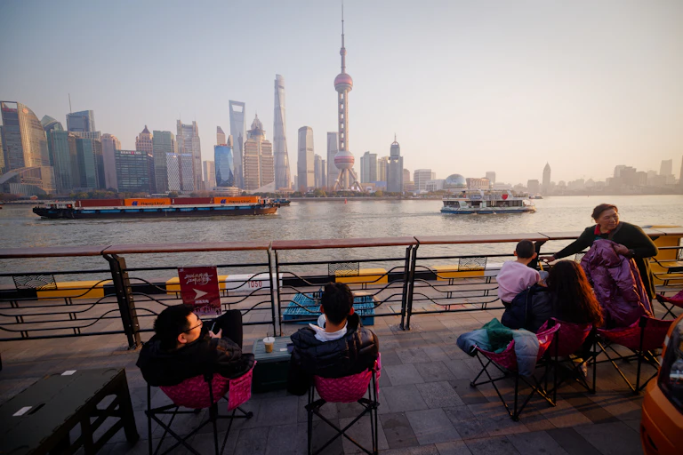 People in cafe watch cargo ships passing by on Huangpu River, in Shanghai, China