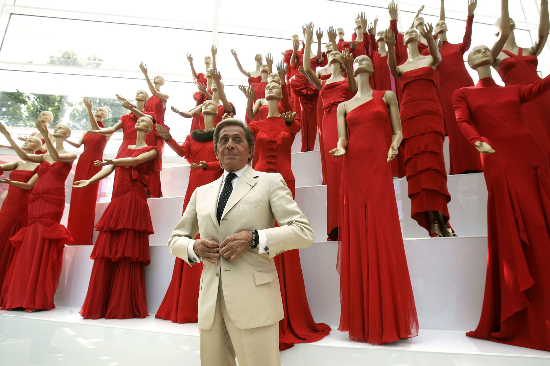 Valentino in front of many mannequins in red dresses. 