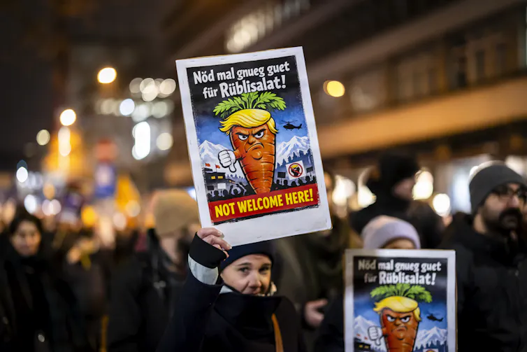 A protester holds a placard showing a caricature of US President Donald Trump and reading 'Not welcome to here!' during a rally against the World Economic Forum