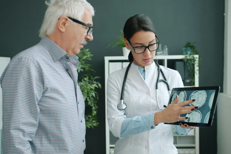 A health care worker showing a man with grey hair a tablet displaying brain scans