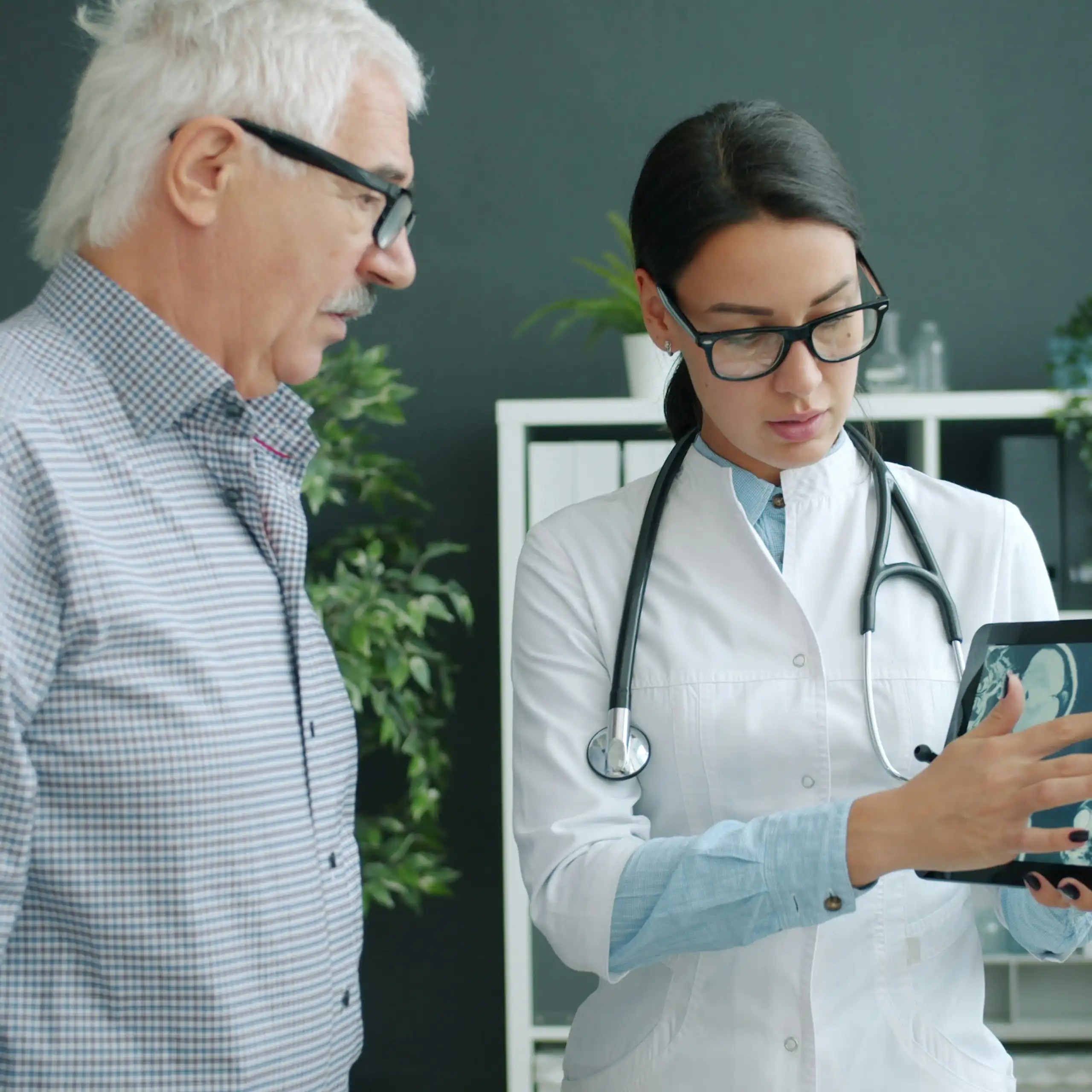 A health care worker showing a man with grey hair a tablet displaying brain scans