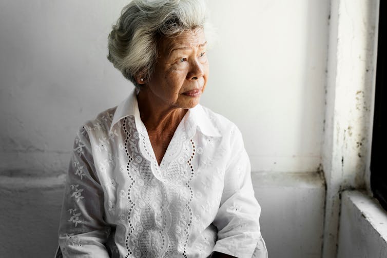 A woman with gray hair in a white blouse sitting at a window