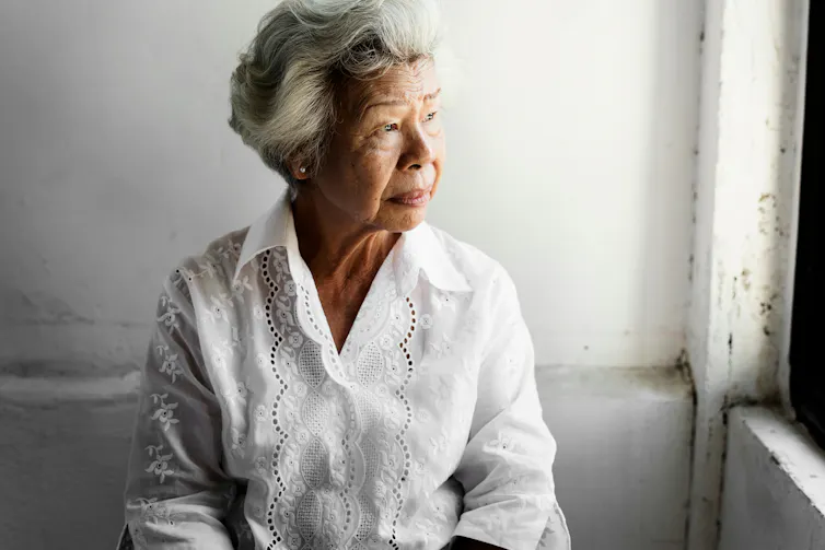 A woman with gray hair in a white blouse sitting at a window