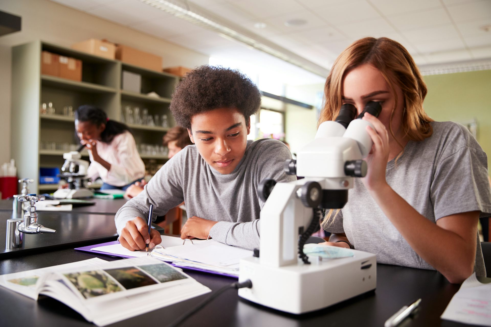 Two students studying, one looking into a microscope.