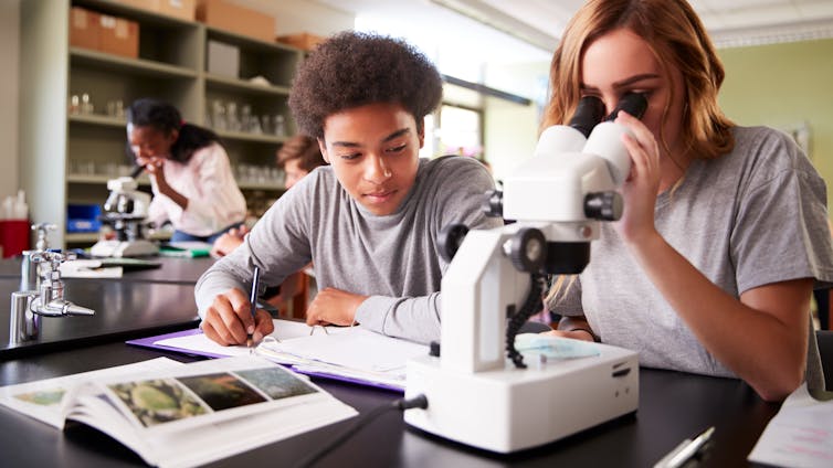 Two students studying, one looking into a microscope.