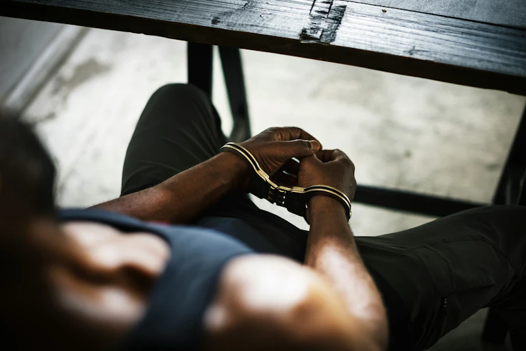 a man photographed from behind sitting in a jail cell with handcuffs on