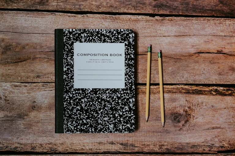 Exercise book and pencils on wooden surface