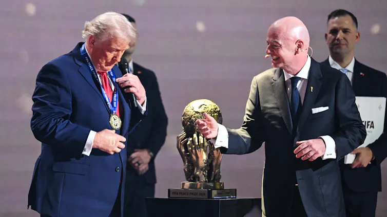 A man in a suit looking down at a medallion on a ribbon he's just put on as others look on.