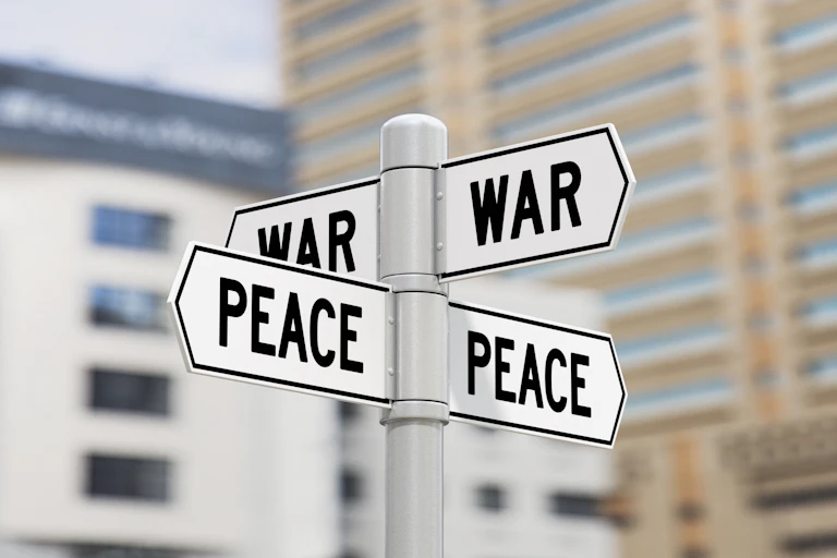 Two intersecting street signs, one saying 'WAR' and the other saying 'PEACE.'
