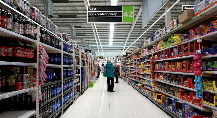 a shopper walks down a supermarket aisle stocking fizzy drinks and sweets.