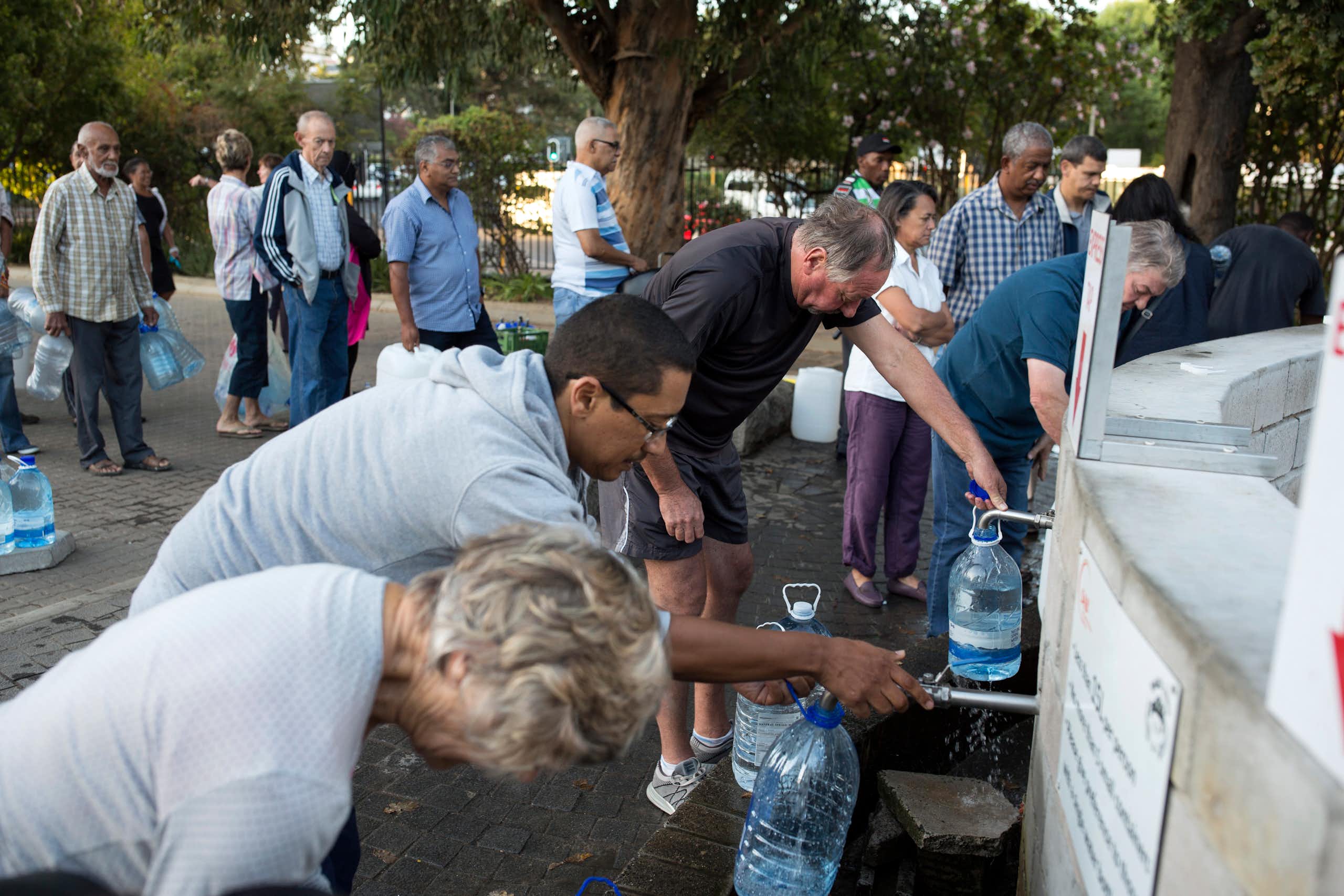 Pessoas de todas as origens fazem fila com jarros para encher com água.
