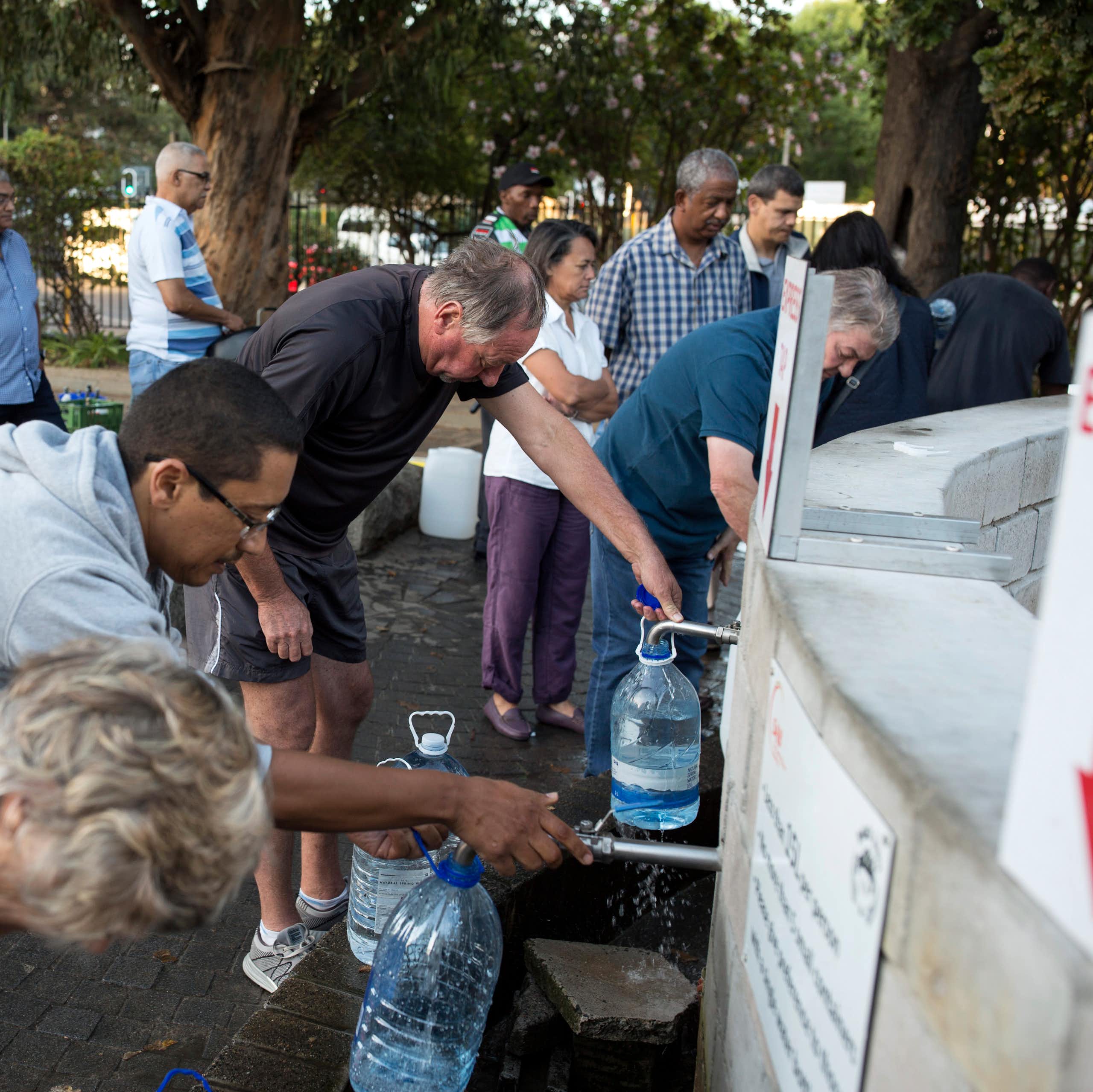 Pessoas de todas as origens fazem fila com jarros para encher com água.
