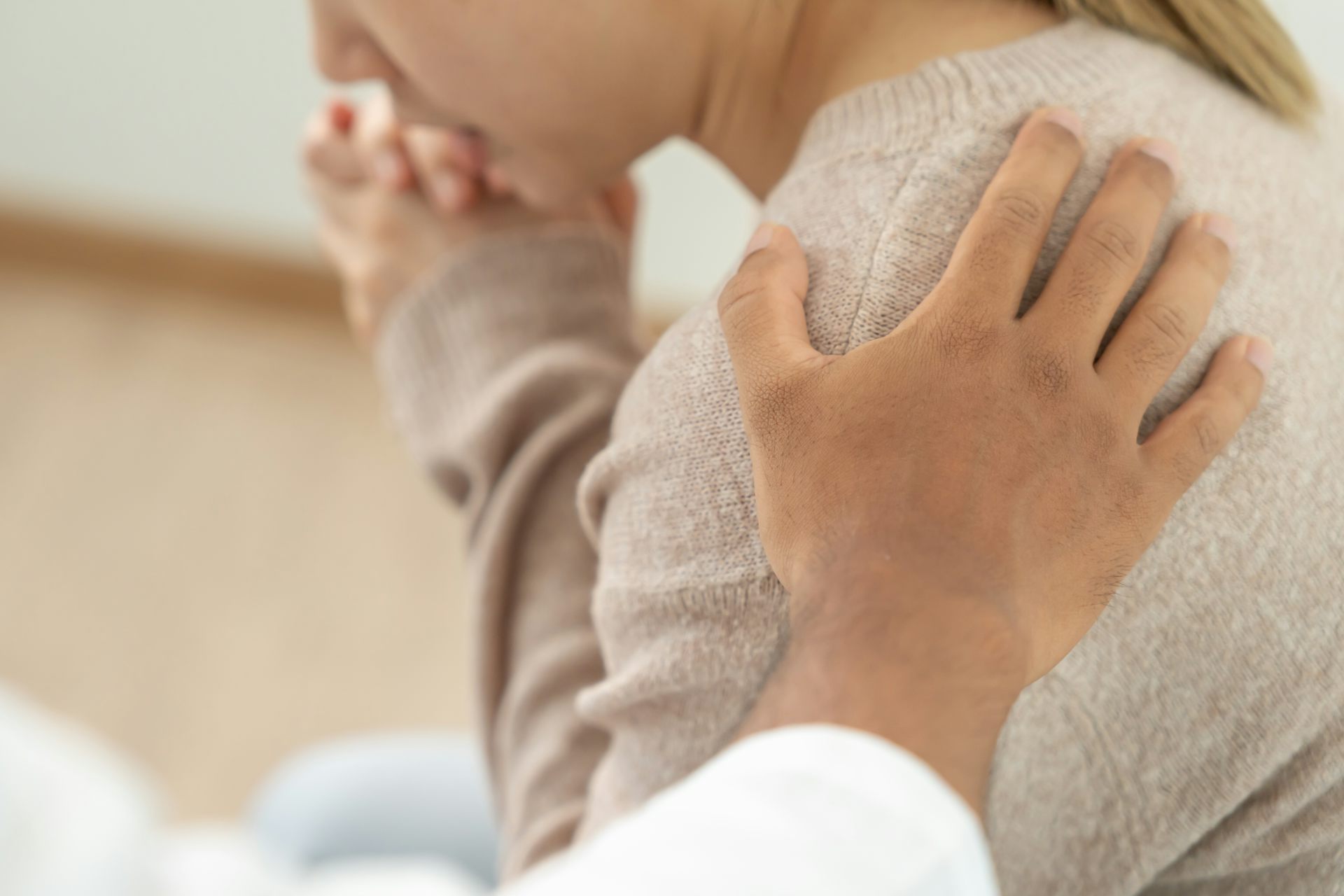 Mano posada sobre el hombro de una mujer con gesto de sufrimiento.