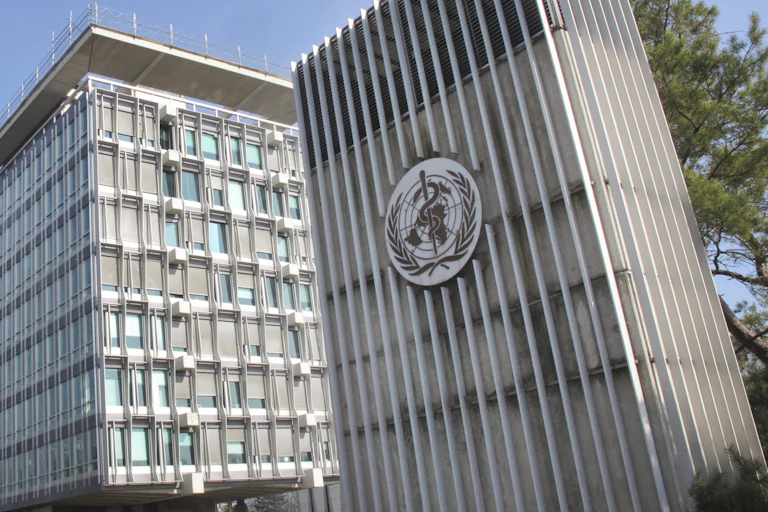 Two grey buildings, one of which bears the round seal of the World Health Organization
