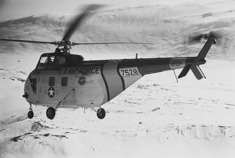 A U.S. Air Force helicopter flies over snow.