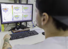 Foto mostra pessoa de costas olhando para a tela do computador onde se vêem mapas