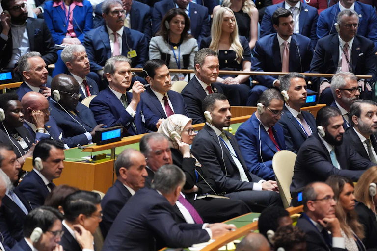 Dozens of people sit in a hall and listen to a person speak.