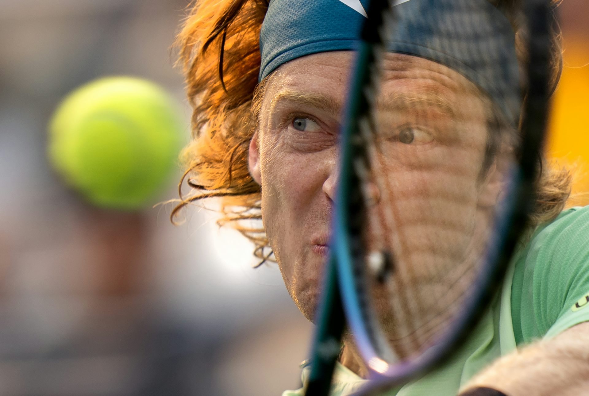 Close up of a tennis player's face scrunched up in concentration as he hits the ball