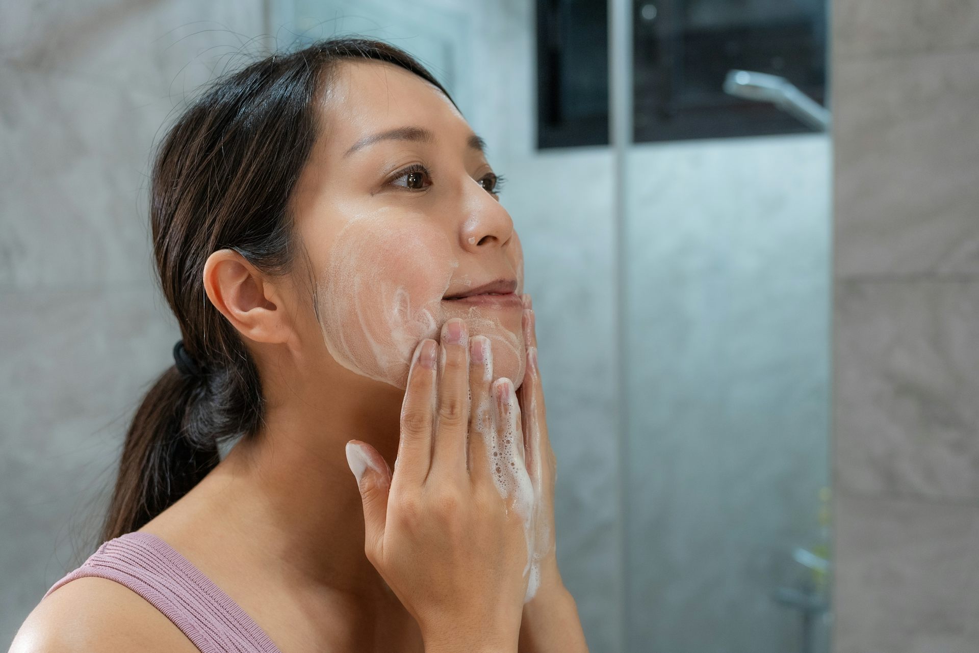 A woman uses a cleanser to clean her face.