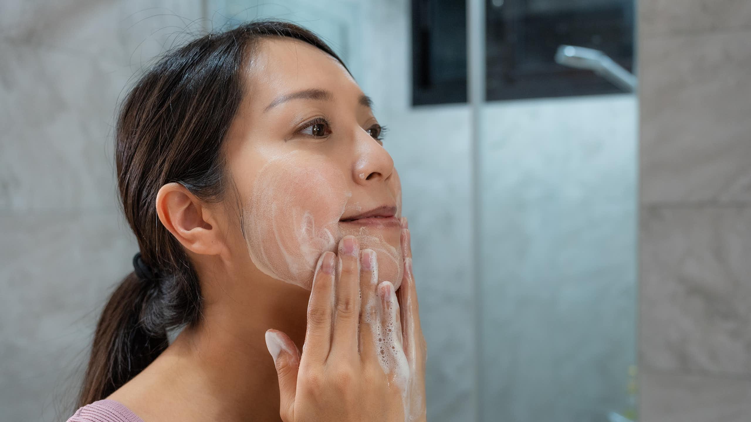 A woman uses a cleanser to clean her face.