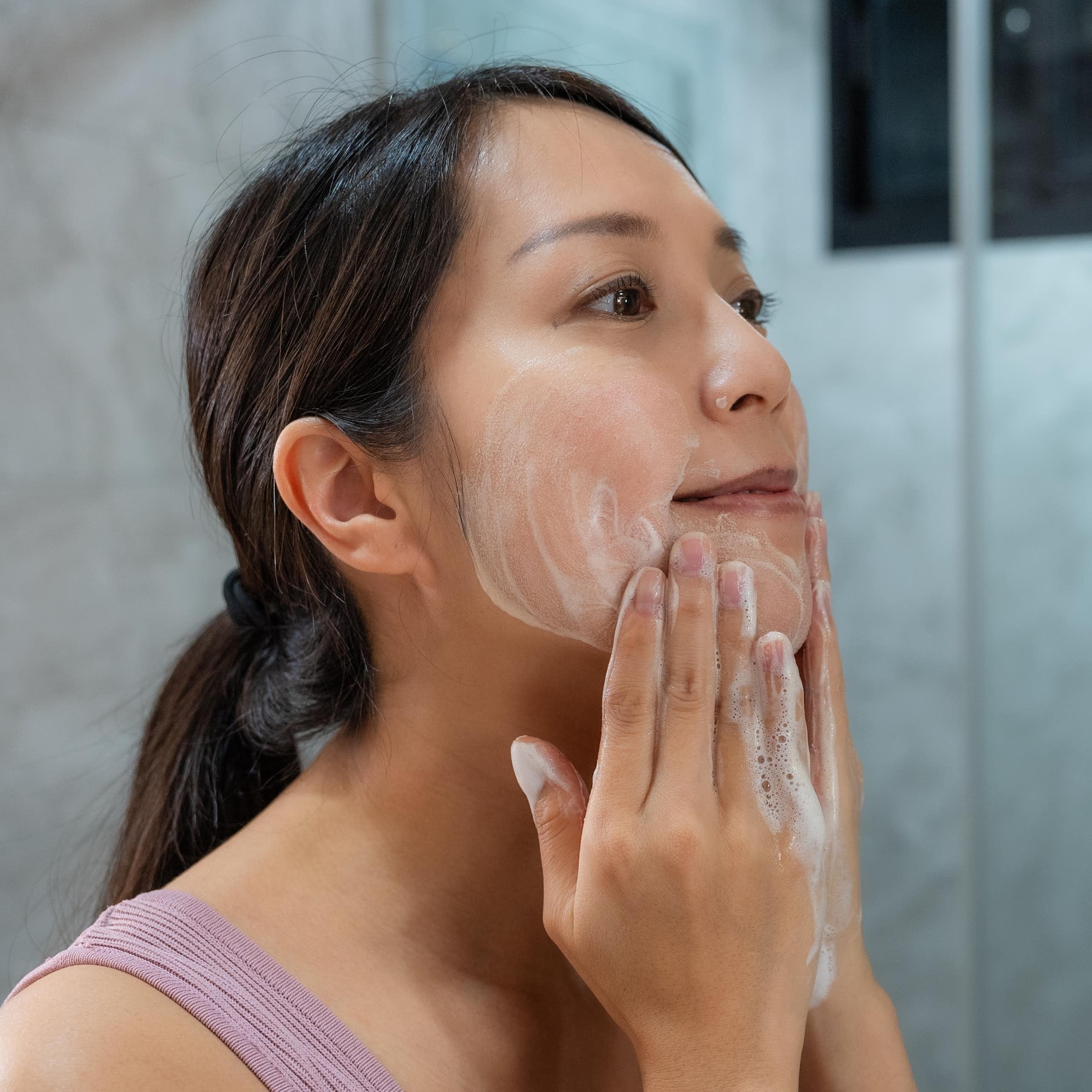 A woman uses a cleanser to clean her face.