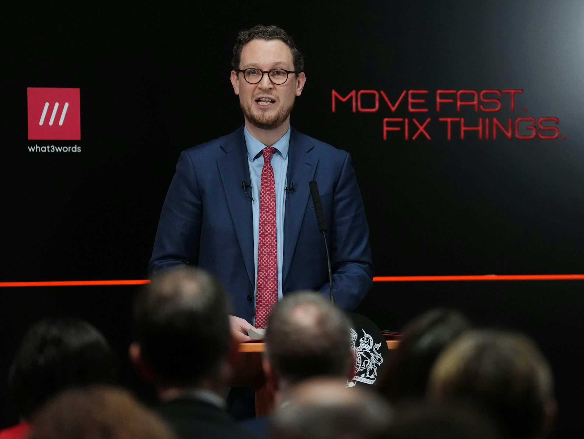 Darren Jones at lectern in front of black background