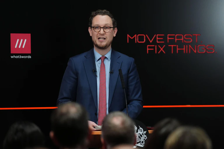 Darren Jones at lectern in front of black background