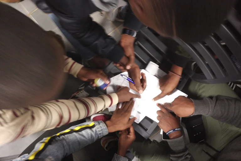 View from above of hands pointing to pieces of paper; one is holding a pen