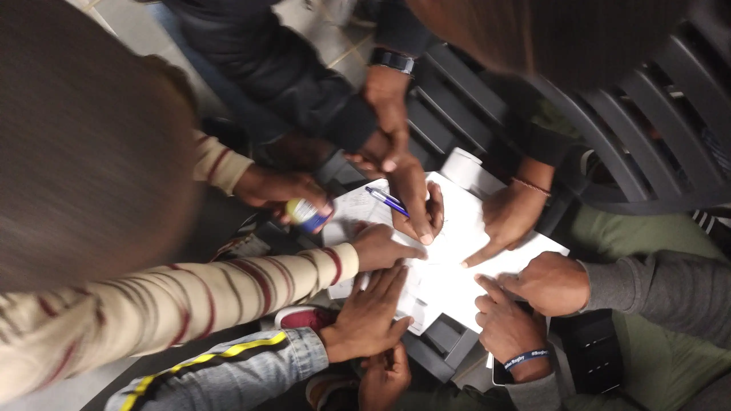 View from above of hands pointing to pieces of paper; one is holding a pen