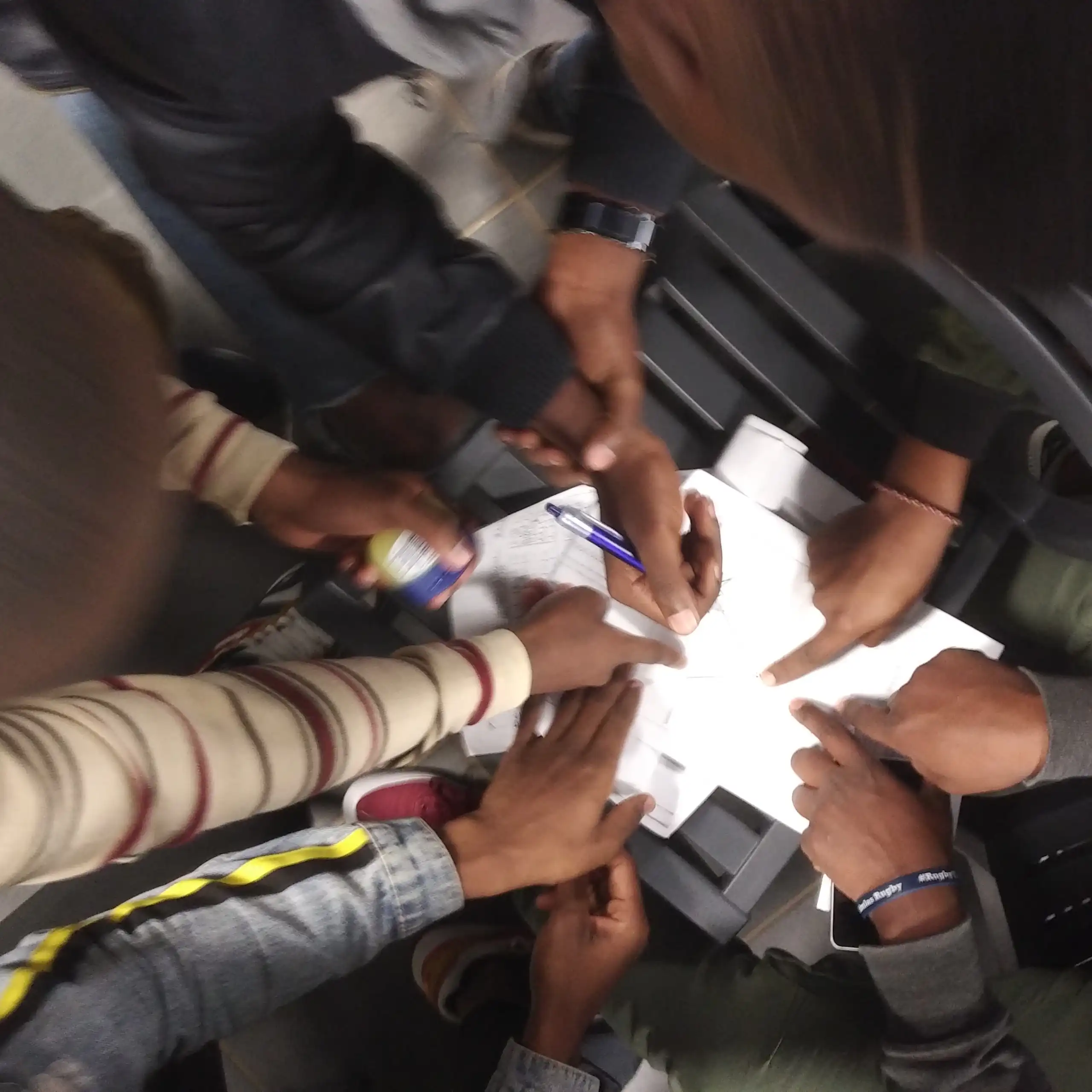 View from above of hands pointing to pieces of paper; one is holding a pen