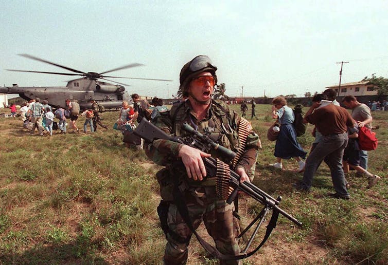 A soldier tells people to get into a helicopter.