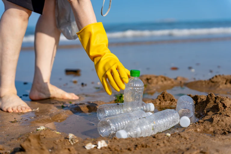 A hand picking up plastic bottles on a beach.