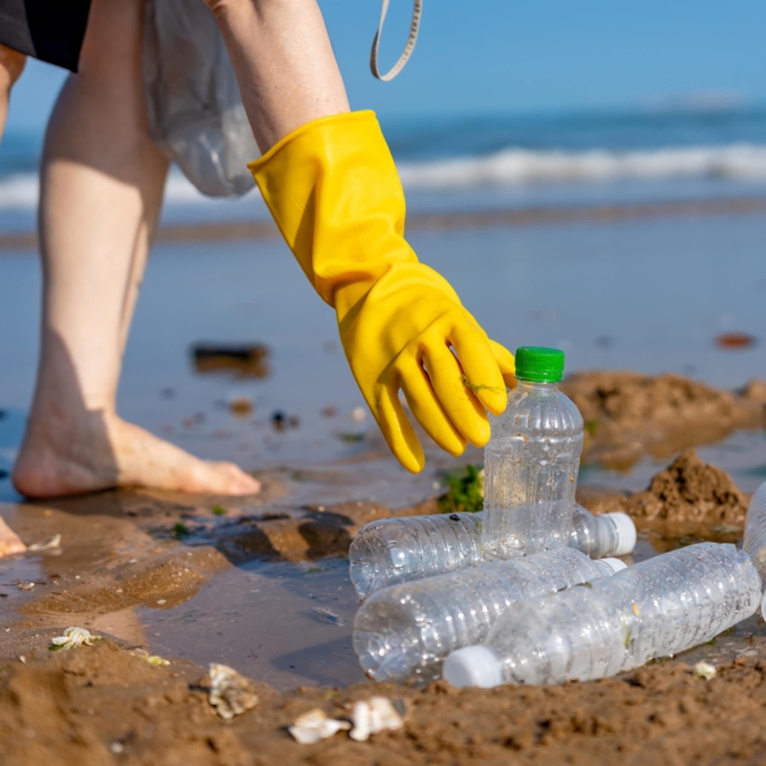 A hand picking up plastic bottles on a beach.