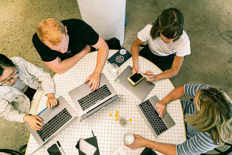 A group of colleagues work together with laptops at a table.