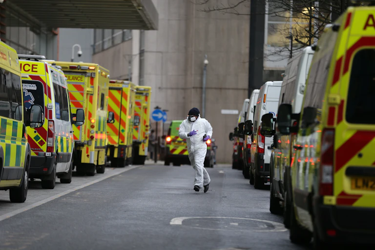 An emergency staff wearing PPE runs through parked ambulances outside Royal London Hospital.