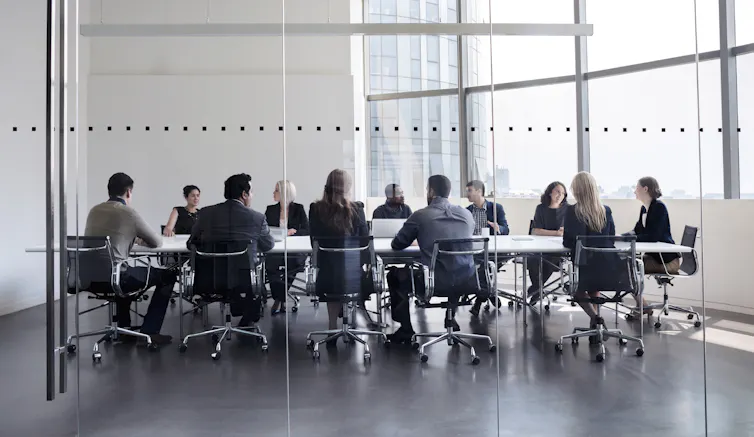 people seated around a meeting-room table seen through a glass wall